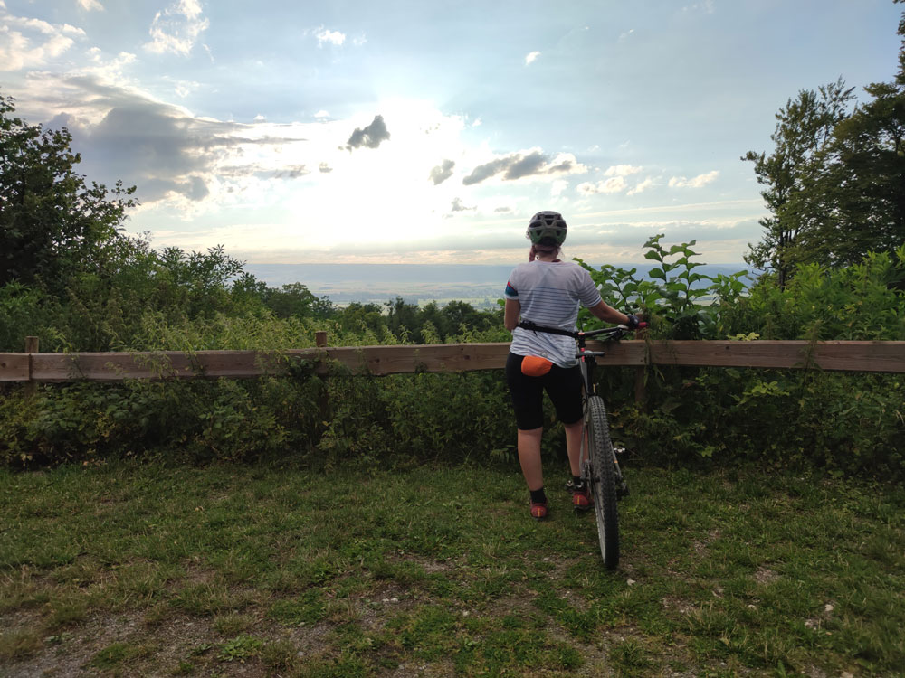 Lisa mit dem Mountainbike und am Rücken ist ein oranges Säckchen zu sehen, in der eine Regenjacke verpackt ist.